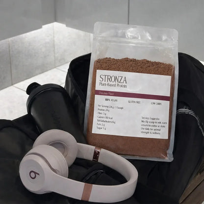 Stronza chocolate plant-based protein powder with shaker and headphones in a gym bag